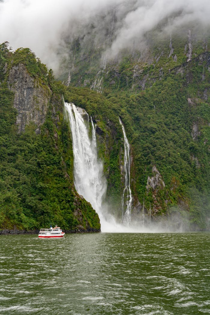 Tour boat approaches stunning waterfall in a mist-covered fjord, capturing nature's grandeur and serene beauty.